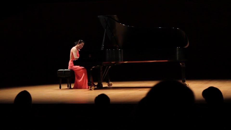 Soojin Jin playing a grand piano on a darkened concert stage